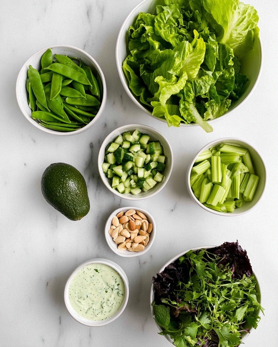 The image shows several white bowls on a white marbled surface, each filled with fresh ingredients. The largest bowl at the top right contains green romaine lettuce leaves. To the left is another large bowl filled with green sugar snap peas. Below these, a smaller bowl holds chopped cucumber pieces, while another on the right contains sliced celery. At the bottom right, a white bowl is filled with mixed leafy greens, including dark and light green leaves. Below the bowls are a whole avocado and a small bowl with a creamy light green dressing with visible herb bits. The smallest bowl at the bottom center holds sliced almonds. All items are arranged neatly, showing a fresh and healthy selection of salad ingredients. Photo taken with an iphone --ar 4:5 --v 7