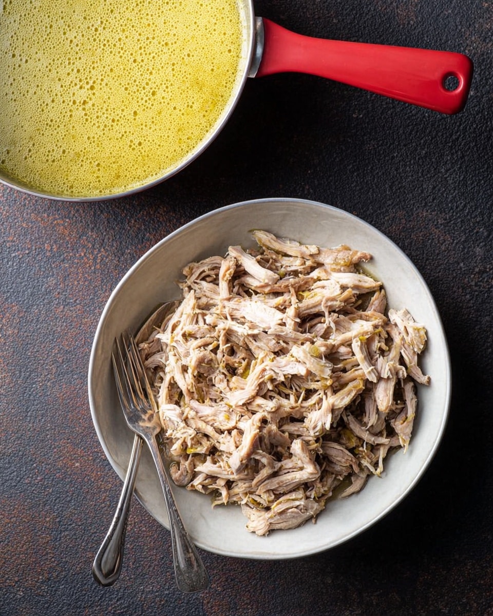 A white round bowl filled with shredded light beige cooked meat, showing some small yellowish pieces mixed in; two silver forks rest on opposite sides of the bowl, one partially inside the meat. Above the bowl is a cookware with a bright red handle, filled with a thick, pale yellow sauce with a slightly frothy texture on top. The background is a dark textured surface, contrasting with the white bowl and colorful sauce container. Photo taken with an iphone --ar 4:5 --v 7