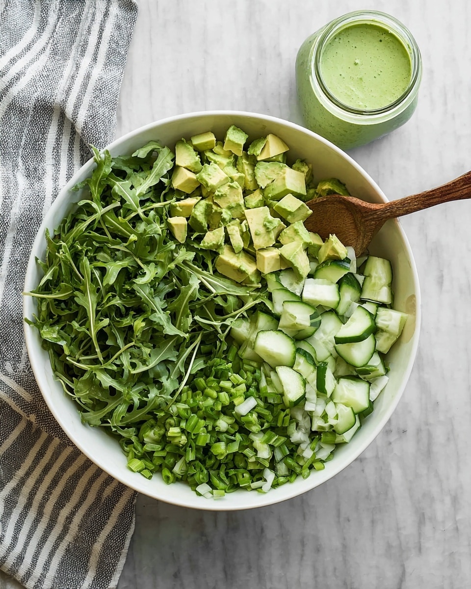 The image shows a white bowl with four layers of fresh green ingredients arranged separately. The bottom left quarter has dark green arugula leaves with a slightly rough texture. The top left quarter contains small, light green avocado cubes with soft edges. The top right quarter features thin pieces of cucumber with a bright green skin and pale green inside. The bottom right quarter is filled with chopped green onions and lettuce, showing different shades of green with small round shapes. Next to the bowl is a small glass jar with a green creamy dressing and a wooden spoon inside. The background is a white marbled texture. Photo taken with an iphone --ar 4:5 --v 7