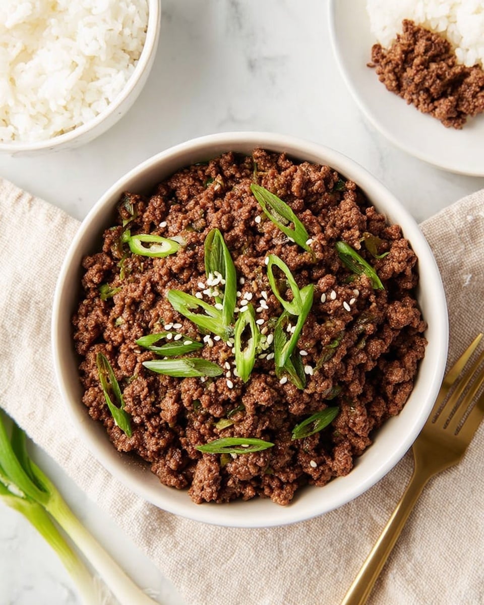 A white bowl filled with cooked ground beef that has a rich brown color and crumbly texture, topped with thinly sliced bright green onions and white sesame seeds, sitting on a beige cloth over a white marbled surface. Around the bowl, there is a small white bowl of steamed white rice on the left side, and a white plate with some rice and a small portion of the ground beef on the right side. A gold fork rests on the beige cloth near the bowl. Photo taken with an iphone --ar 4:5 --v 7