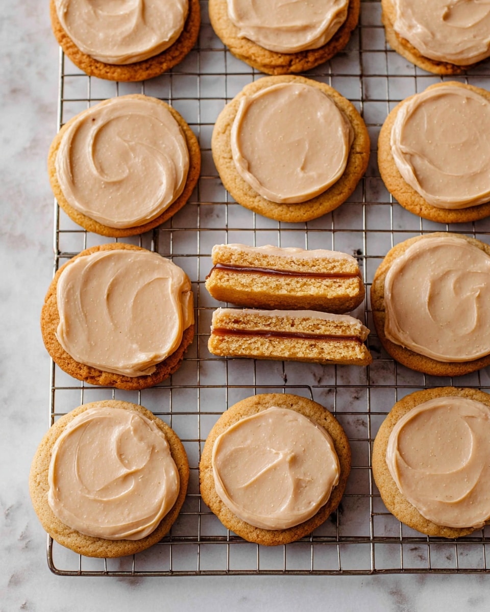 There are twelve round cookies on a metal cooling rack over a white marbled surface. Each cookie has one layer with a light brown smooth frosting spread evenly on top. One cookie is cut in half, showing two layers: the top layer is a light brown frosting, the bottom layer is a golden brown cookie, and a dark brown filling in the middle. The cookies have a soft and slightly thick texture with smooth edges. Photo taken with an iphone --ar 4:5 --v 7