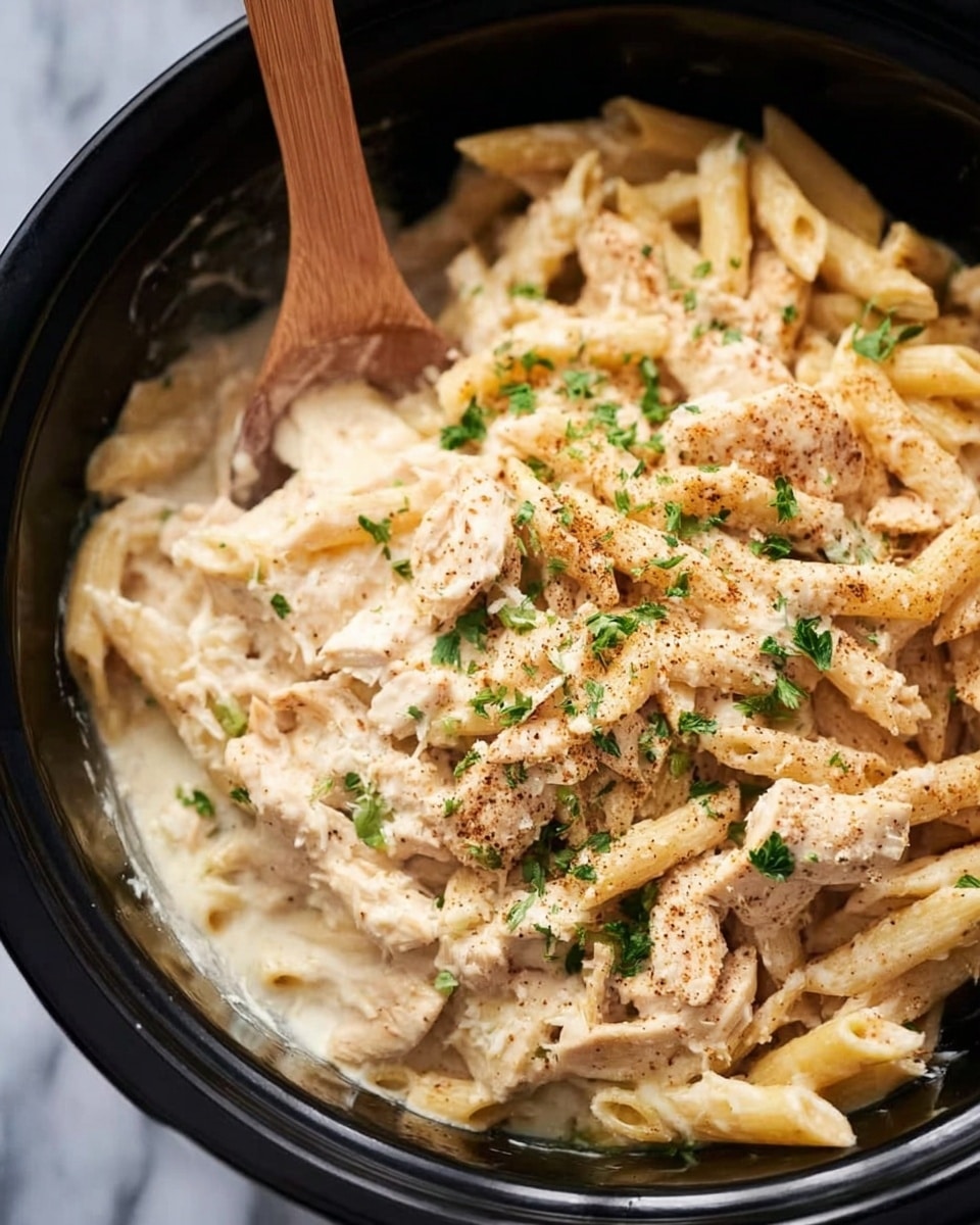 A black bowl filled with creamy pasta shows about two layers: the bottom layer has cooked penne pasta in a smooth white sauce, and the top layer has pieces of tender chicken mixed evenly with the pasta. The entire dish is sprinkled with light brown seasoning powder and some small green herb bits. A wooden spoon rests inside the bowl, leaning toward the left side, partially covered in sauce. The bowl sits on a white marbled surface photo taken with an iphone --ar 4:5 --v 7