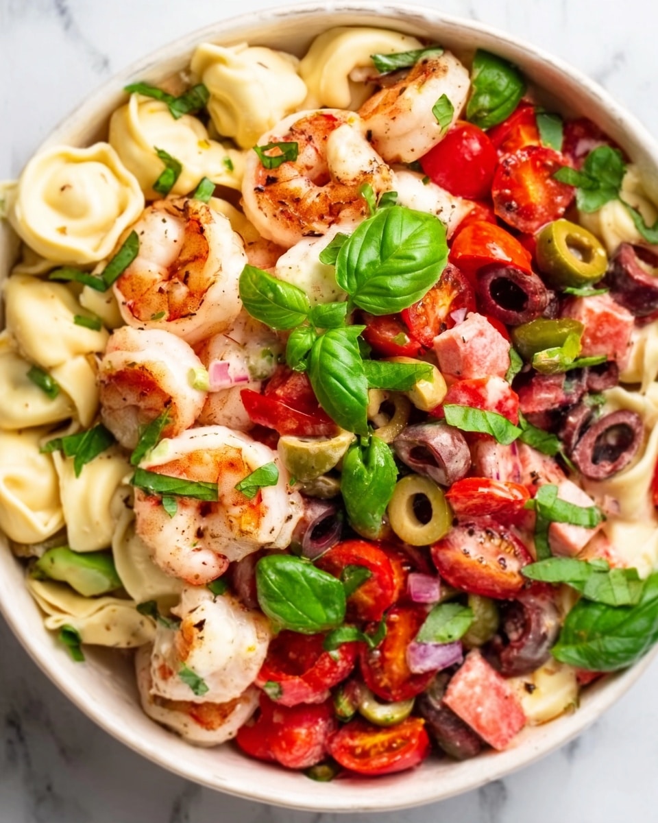 This image shows a white bowl filled with a colorful shrimp salad on a white marbled surface. The salad has three main layers: a base of small, folded tortellini pasta pieces in a light cream color, followed by a mixture of pink and red diced tomatoes, black and green olives, and pieces of pale shrimp scattered on top. Bright green basil leaves are spread across the salad, adding fresh color and texture. The shrimp have a slightly grilled look with a light brown color on one side. The photo taken with an iphone --ar 4:5 --v 7