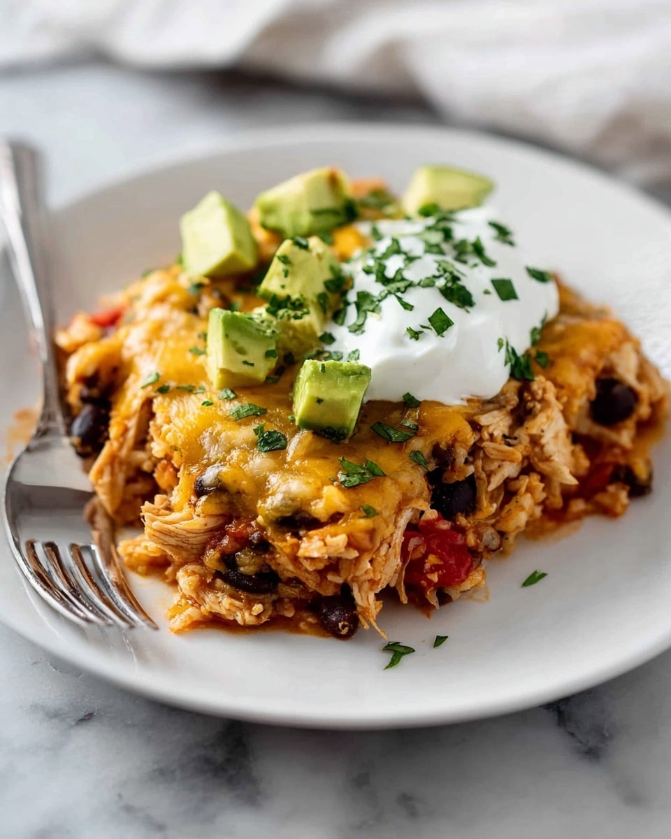 A white plate holds a layered dish with a base of shredded chicken mixed with black beans, rice, and small chunks of red tomatoes. On top of this is a golden layer of melted cheese, slightly browned in spots. Garnished on top are small cubes of bright green avocado and a generous dollop of white sour cream sprinkled with chopped green herbs. The plate is set on a white marbled surface, with a fork resting on the left side of the plate. Photo taken with an iphone --ar 4:5 --v 7