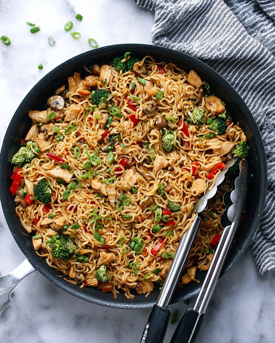 A large black pan filled with cooked noodles mixed with small pieces of light brown chicken, bright green broccoli florets, chopped red bell peppers, and sliced brown mushrooms, all evenly spread throughout. Thinly chopped green onions are scattered on top adding a fresh green touch. The noodles look soft with a slight shine from the sauce coating them. A pair of black and silver tongs rests on the right side inside the pan. The pan is placed on a white marbled surface with a folded gray and white striped cloth in the upper right corner. Photo taken with an iphone --ar 4:5 --v 7