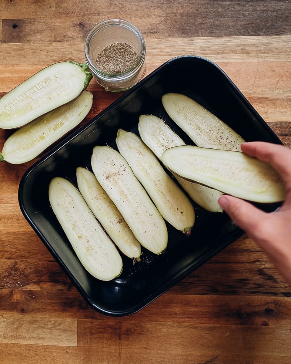 The image shows a black rectangular tray with four long, thin slices of eggplant inside, placed on a wooden surface with a glass jar of seasoning next to it. To the left of the tray, several more eggplant slices are stacked neatly in a row. A woman's hand is holding one slice of eggplant over the right side of the tray. The eggplant slices are pale green with visible seeds and slight speckles on the surface. photo taken with an iphone --ar 4:5 --v 7