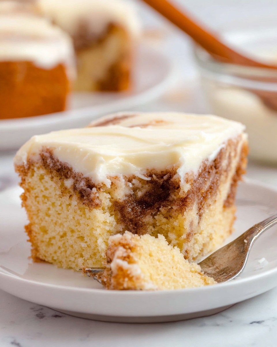 A slice of moist cinnamon swirl cake sits on a white plate on a white marbled surface, showing two main layers: the bottom layer is a soft, light yellow cake mixed with swirls of cinnamon spice creating a marbled brown pattern, while the top layer is a thick, smooth, creamy white frosting spread evenly over the cake. A silver fork is lifting a piece from the right edge of the slice, digging into the cake and frosting, with a blurred background including another white plate with cake and a glass bowl with a wooden spoon. photo taken with an iphone --ar 4:5 --v 7