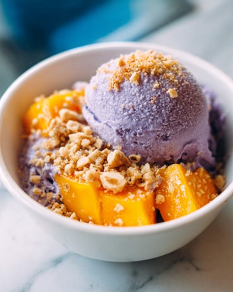 A white bowl with a pale green pattern holds a scoop of smooth purple ice cream on the left side. The ice cream scoop is sprinkled with small golden brown crumbs. Next to the ice cream on the right side, there are orange-yellow pieces of soft mango, also topped with a few crumbs. The bowl is set on a white marbled surface. photo taken with an iphone --ar 4:5 --v 7