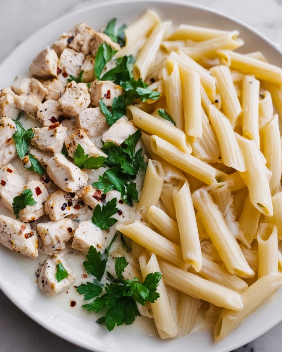 The image shows a close-up of a white plate with cooked plain penne pasta on the right side, displaying a smooth, light yellow color and a slightly glossy texture. On the left side of the plate, there are small pieces of white cooked chicken meat, seasoned with black pepper and chili flakes, creating small dark and reddish spots. Fresh green parsley leaves are scattered on and around the chicken, adding a bright color contrast. The plate is set on a white marbled surface. photo taken with an iphone --ar 4:5 --v 7