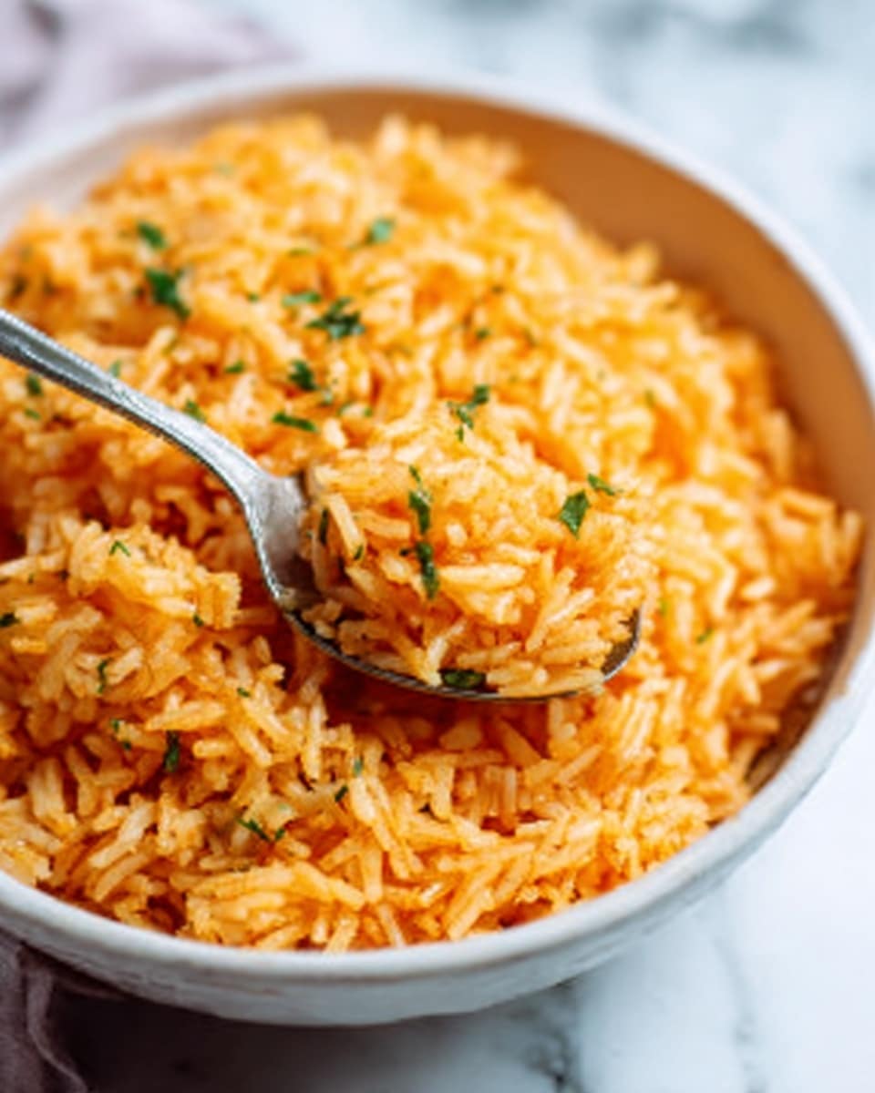 A close-up view of a white metal pot filled with cooked rice mixed with small pieces of red tomatoes and green herbs. The rice has a slightly glossy, soft texture with a reddish-orange color from the sauce. A gold spoon is inside the pot, partially lifted showing the thick, mixed rice. The pot sits on a white marbled surface with a white cloth nearby. Photo taken with an iphone --ar 4:5 --v 7