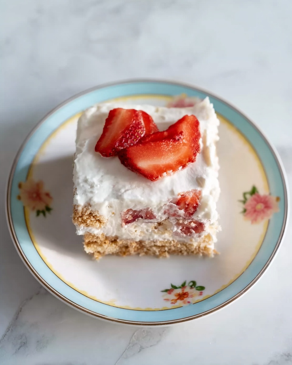 The image shows a single square slice of dessert on a white plate with a pastel blue and yellow rim and small floral patterns. The dessert has three visible layers: the bottom layer is a crumbly, light brown crust, the middle layer contains pieces of red strawberries mixed into a white creamy filling, and the top layer is smooth white cream with a few thin strawberry slices on top. The plate is placed on a white marbled surface. The photo taken with an iphone --ar 4:5 --v 7