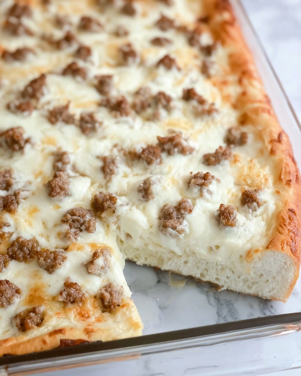 The image shows a thick rectangular white pizza with two layers visible in a glass tray. The bottom layer is a thick and soft white bread crust, fluffy in texture. The top layer is creamy melted cheese spread evenly, topped with small pieces of cooked brown sausage sprinkled all over. One slice is slightly pulled away on the right side, showing the layers clearly. The background is a white marbled texture. Photo taken with an iphone --ar 4:5 --v 7