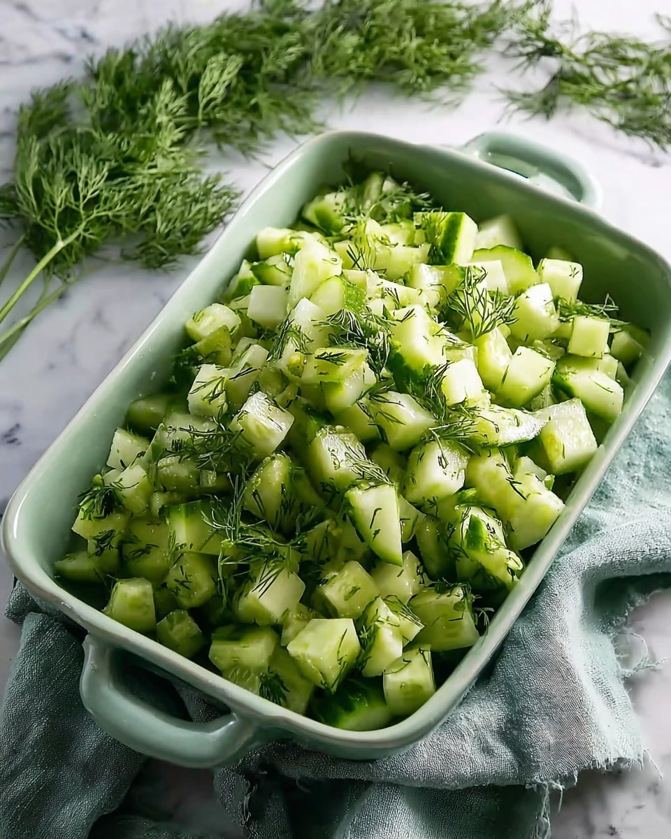 A light green rectangular ceramic dish filled with small, uneven cubes of pale green cucumber mixed with sprigs and small pieces of fresh dark green dill, creating a fresh, textured look. The dish sits on a soft sage-green cloth, on a white marbled surface, with more fresh dill placed casually in the background, adding to the fresh and healthy feel of the image. Photo taken with an iphone --ar 4:5 --v 7