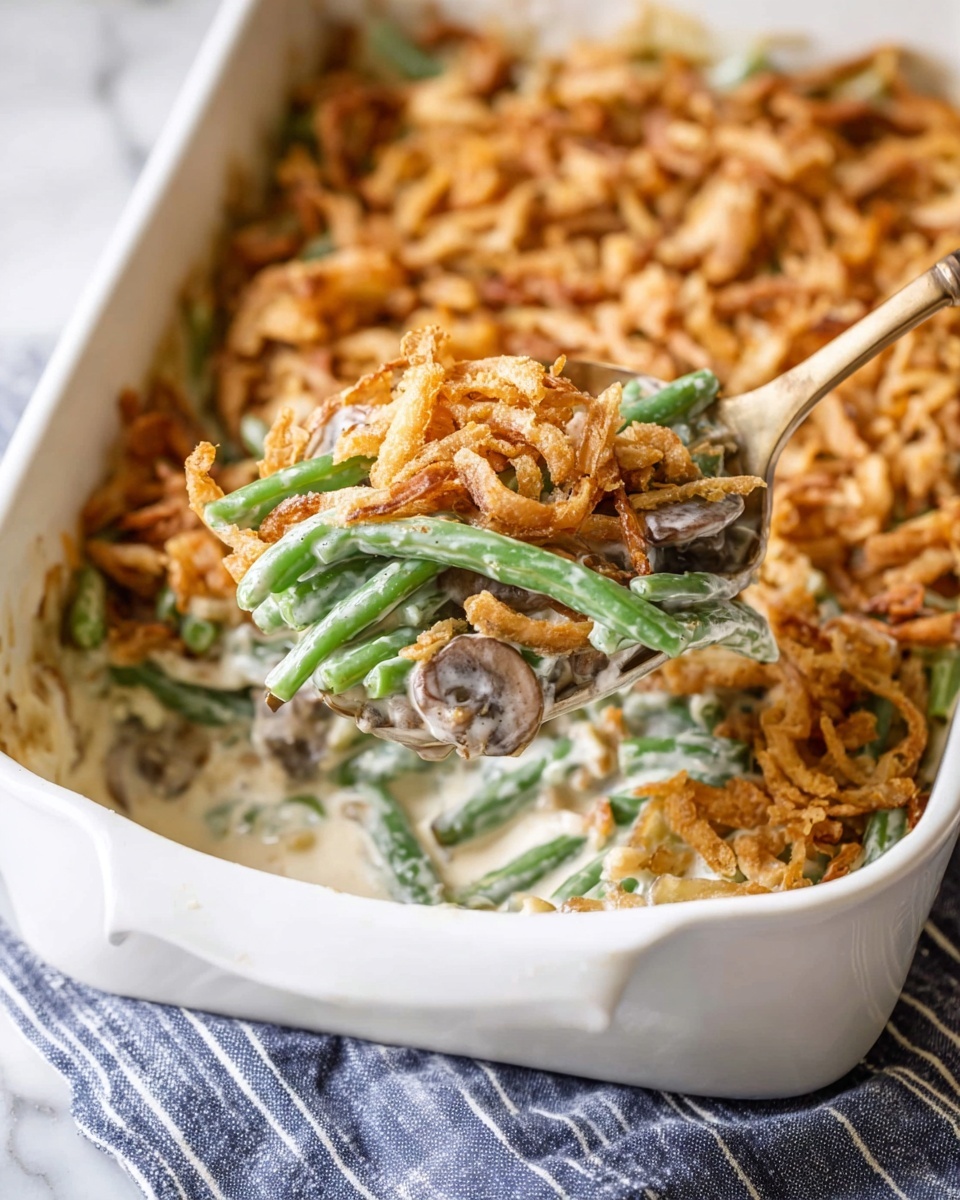 A white baking dish filled with green bean casserole, showing three layers: the bottom creamy layer with white sauce and pieces of light brown mushrooms, the middle layer of bright green beans mixed with the sauce, and the top layer of crispy golden brown fried onion strips covering the surface. A light-colored spoon lifts a scoop revealing all three layers with the creamy texture and crunchy topping visible. The dish is set on a blue-striped cloth with a white marbled surface in the background. photo taken with an iphone --ar 4:5 --v 7