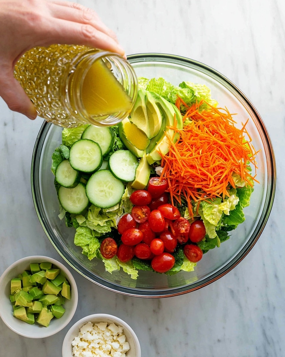 A clear glass bowl sits on a white marbled surface filled with fresh green lettuce leaves as the base layer. On top, there are three more layers: thinly shredded bright orange carrots arranged in a small pile on one side, sliced light green cucumbers with dark green edges placed next to the carrots, and halved red cherry tomatoes grouped together on another side. A woman's hand is pouring a golden yellow dressing from a patterned glass jar over the salad. Below the bowl, on the white marbled surface, there are two small white bowls: one filled with chopped green avocado pieces and the other with small white crumbly cheese. photo taken with an iphone --ar 4:5 --v 7