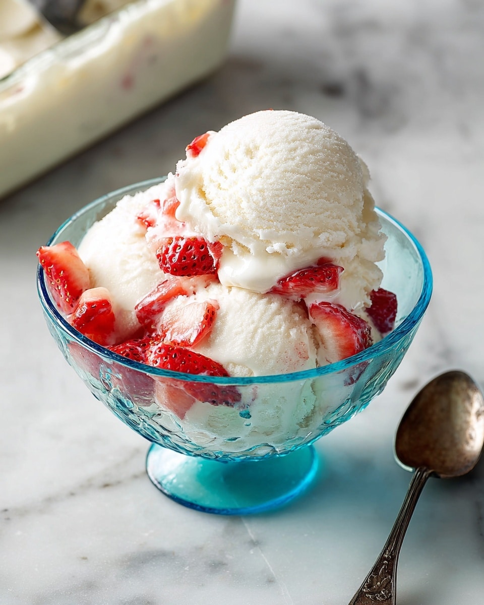 A clear blue glass bowl holds two large scoops of smooth white ice cream, topped and mixed with small red strawberry pieces that add vibrant color and texture. The bowl is set on a white marbled surface with a tarnished silver spoon next to it. In the blurred background, an ice cream container with a scoop is partly visible. The scene is bright and clean, focusing on the simple layers of creamy ice cream and fresh fruit photo taken with an iphone --ar 4:5 --v 7