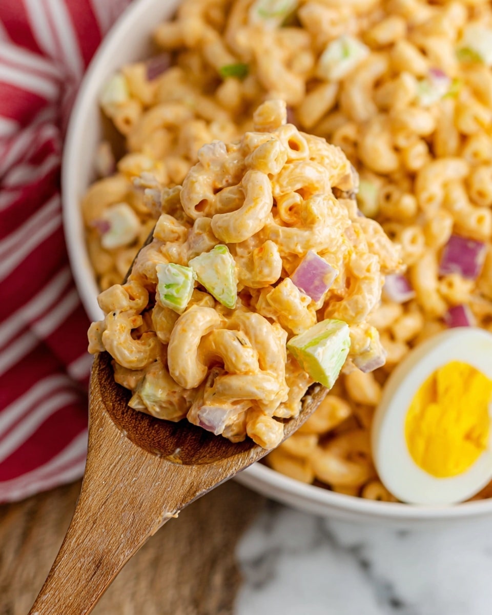 A close-up view of a wooden spoon lifting a scoop of creamy macaroni salad from a white bowl. The salad has three visible layers: the macaroni pasta coated in a smooth, light orange dressing as the main base, small chunks of pale green celery and white boiled egg pieces mixed evenly throughout, and tiny bits of purple onion adding texture. In the background, the rest of the bowl shows more of the macaroni salad with a partial view of a halved boiled egg with a bright yellow yolk on the right side. The scene is set on a white marbled surface with a red and white striped cloth peeking from the lower left corner. photo taken with an iphone --ar 4:5 --v 7