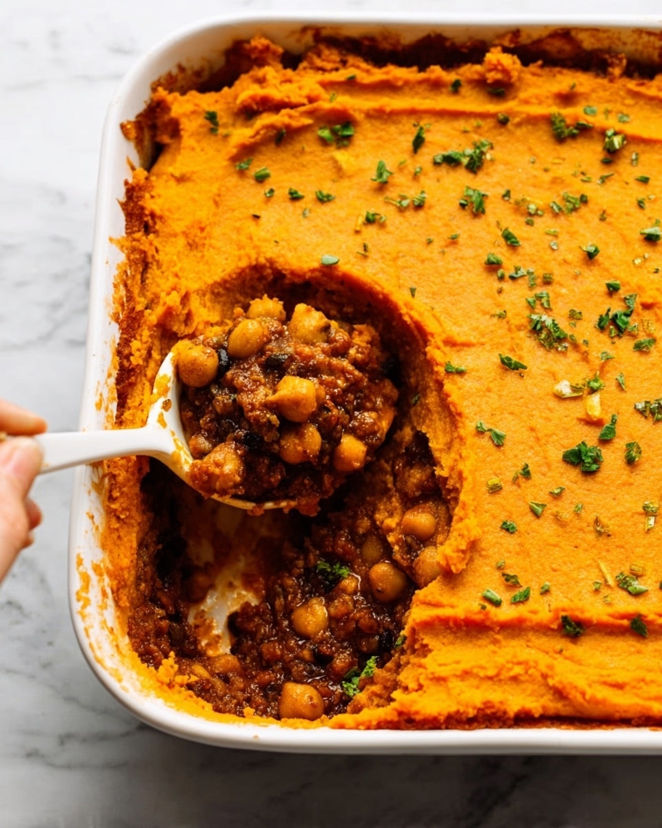 The image shows a white rectangular baking dish filled with a layered casserole. The top layer is thick and smooth with an orange color, sprinkled lightly with small green herb pieces for garnish. Beneath this layer is a dark brown mixture with visible chickpeas, showing a chunky texture. A woman's hand holds a white spoon with some of the chickpeas and sauce, scooping from the corner where a section of the top layer is removed. The dish sits on a white marbled surface. Photo taken with an iphone --ar 4:5 --v 7