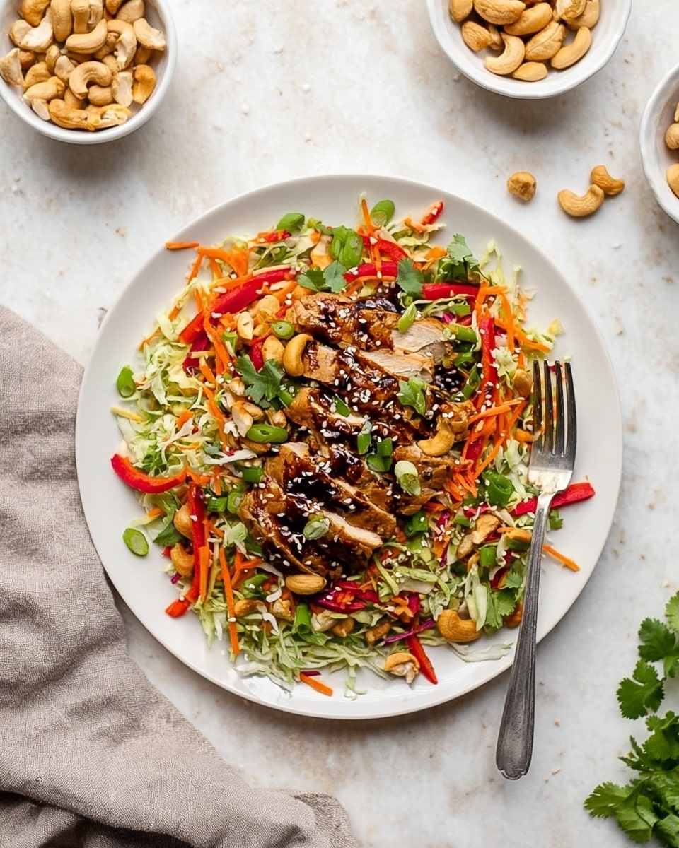 A white plate sits on a white marbled surface with a colorful salad arranged in layers. The bottom layer is shredded cabbage and carrots in green and orange tones, mixed with thin red pepper strips. On top, there are sliced grilled chicken pieces coated with sesame seeds and a dark sauce. Scattered around are sliced green onions, fresh cilantro leaves, thin jalapeno slices, cashew nuts, and sliced almonds adding texture and detail. A fork rests on the right side of the plate, partially placed under the salad. Two white bowls with cashews and sliced almonds are placed in the upper left and right corners, and a light gray cloth is folded at the bottom left. photo taken with an iphone --ar 4:5 --v 7