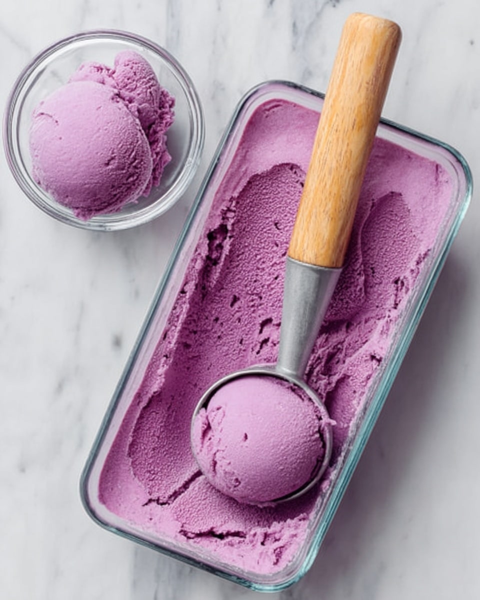 The image shows a rectangular glass dish filled with bright purple ice cream, with a wooden-handled ice cream scooper resting inside. The surface of the ice cream is smooth but has one rounded scoop missing, placed beside the dish in a small clear bowl. The ice cream looks creamy and dense, with the vibrant purple color being the main visual focus. Both containers sit on a white marbled surface. photo taken with an iphone --ar 4:5 --v 7