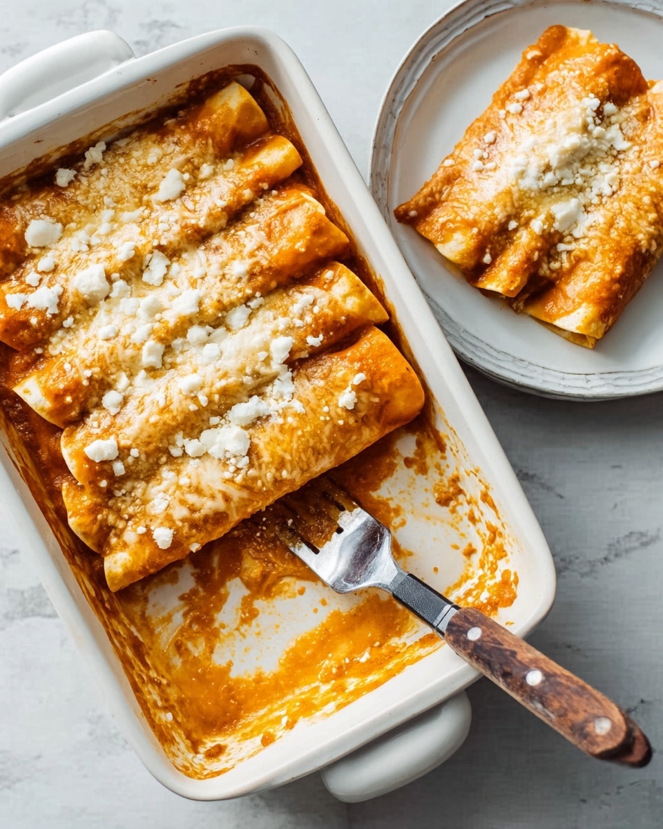 A white rectangular baking dish holds a baked casserole with three rolled layers of soft, slightly browned tortillas filled with an orange sauce. The top is covered with a melted layer of crumbly white cheese that is uneven and textured. Next to the dish, a white round plate shows a single rolled tortilla piece topped with the same sauce and cheese. A fork with a dark handle rests inside the baking dish near the empty space where a piece was taken out. The setting is on a white marbled surface. photo taken with an iphone --ar 4:5 --v 7