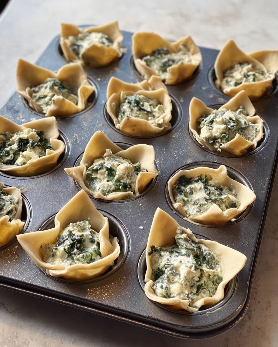 A dark gray metal muffin tray holds 12 cups, each filled with a light beige thin pastry dough shaped like a small cup with uneven edges folding outward. Inside each pastry cup is a creamy white and green mixture that looks like a spinach and cheese filling, with a slightly chunky texture and specks of darker green leaves. The muffin tray sits on a white marbled surface with soft natural light reflecting on the tray’s smooth edge. photo taken with an iphone --ar 4:5 --v 7
