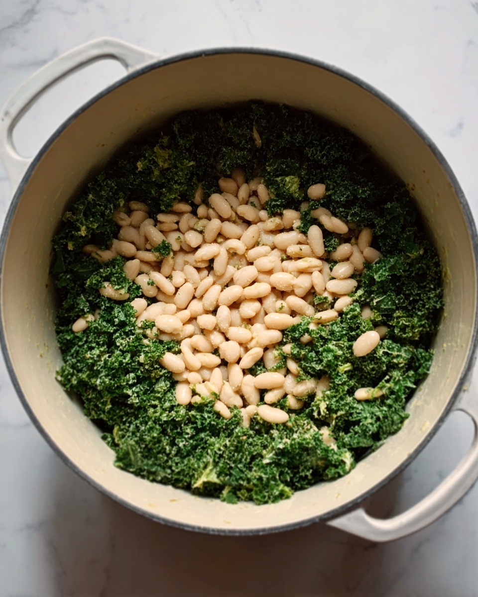 The image shows a close-up of a white pot with two small handles, filled with two layers of ingredients. The bottom layer is finely chopped green kale covering the whole base, and the top layer is small, round white beans spread evenly on top of the kale. The colors contrast between the dark green of the kale and the pale beige of the beans. The pot sits on a white marbled surface. photo taken with an iphone --ar 4:5 --v 7