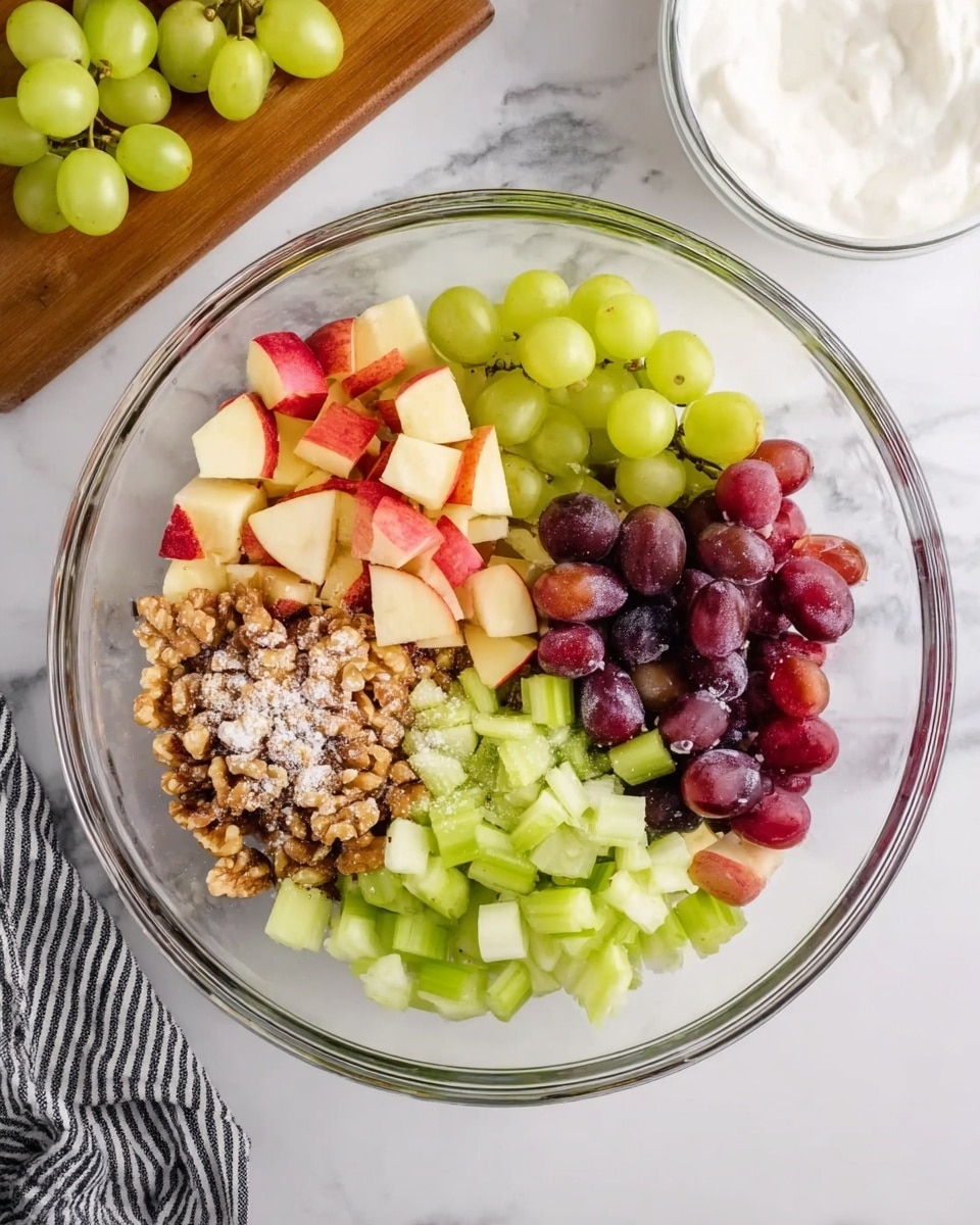The image shows a clear glass bowl with six separate sections of chopped fruit and nuts inside, placed on a white marbled surface. On the top left are small green grapes, next to them diced red-skinned apple pieces. Below the apples are small light green celery cubes, then a section of purple grapes cut in halves at the bottom right. At the bottom left are green apple chunks, and in the middle are crumbled walnuts sprinkled with white sugar. The background includes a wooden board with whole green grapes on the top left and a clear bowl with white yogurt on the top right. A black and white striped cloth is at the bottom left corner of the scene. Photo taken with an iphone --ar 4:5 --v 7