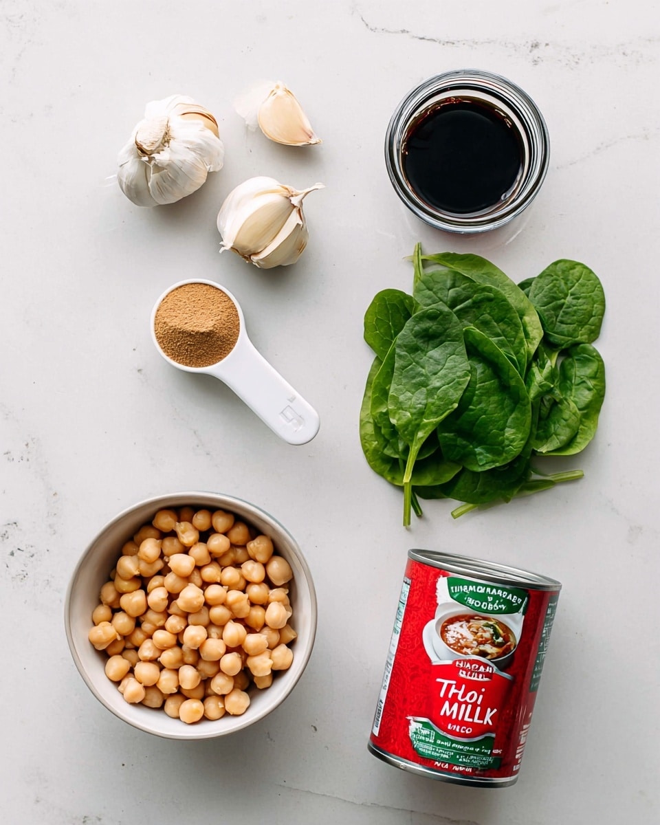 The image shows six separate ingredients on a white marbled surface arranged neatly. At the top left, three peeled garlic cloves are together beside a white measuring spoon filled with light brown powder. Next to them is a small glass jar filled with dark liquid, and to the right, there is a small bunch of fresh green spinach leaves. Below the garlic and spice, a small round white bowl is filled with light beige chickpeas. To the right of the bowl, there is a can of Thai Kitchen Organic coconut milk with a red and green label. A red container of Maesri red curry paste sits between the garlic and chickpeas near the center. The photo taken with an iphone --ar 4:5 --v 7