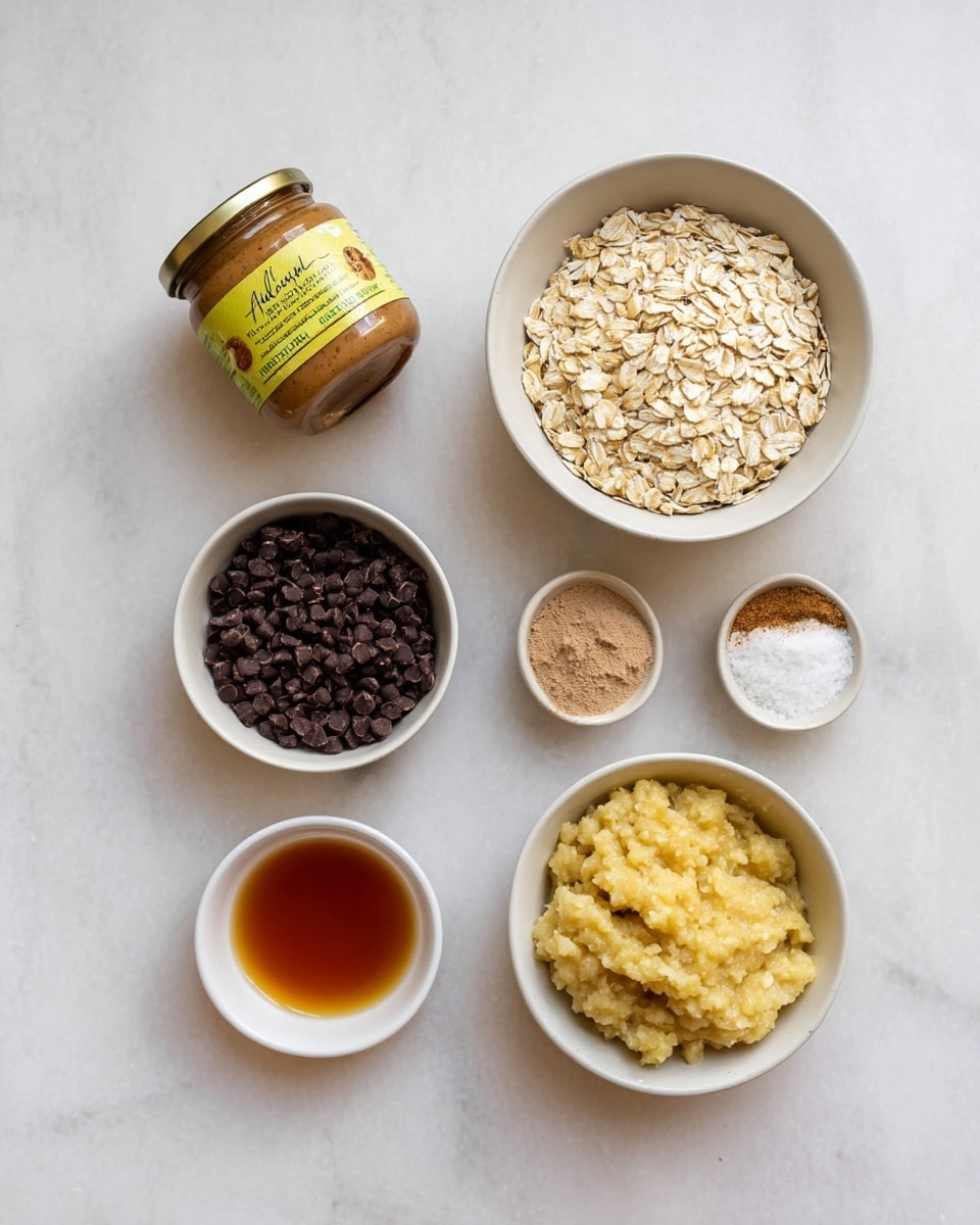 The image shows a top view of six ingredients arranged on a white marbled surface. Starting from the top left is a jar of smooth almond butter with a yellow label, just beside it is a small white bowl filled with light brown rolled oats. To the right of the oats is a small white bowl that holds two light brown powders and a white granular substance. In the bottom left corner is a white bowl filled with dark chocolate chips. Next to it, on the right side, is another white bowl with a light yellow mashed banana mixture. Below the chocolate chips is a tiny white bowl containing amber-colored liquid. Photo taken with an iphone --ar 4:5 --v 7