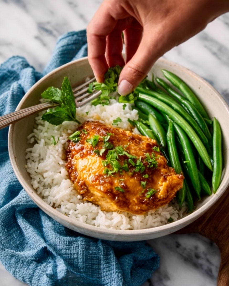 A white bowl filled with a base layer of white rice, topped with a golden-brown cooked chicken piece that has a slightly crispy texture. On one side of the chicken, there is a neat row of bright green steamed green beans. A woman's hand is adding small fresh green herb leaves on top of the chicken as a final touch. The bowl is placed on a white marbled surface with a folded blue cloth nearby. Photo taken with an iphone --ar 4:5 --v 7