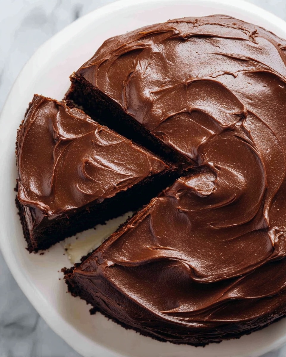 A round chocolate cake with one slice slightly pulled out shows thick, rich, dark brown chocolate frosting spread smoothly and swirled with a glossy texture on top. The cake layer beneath is dark brown, visible from the cut slice. The cake sits on a white plate placed on a white marbled surface. photo taken with an iphone --ar 4:5 --v 7