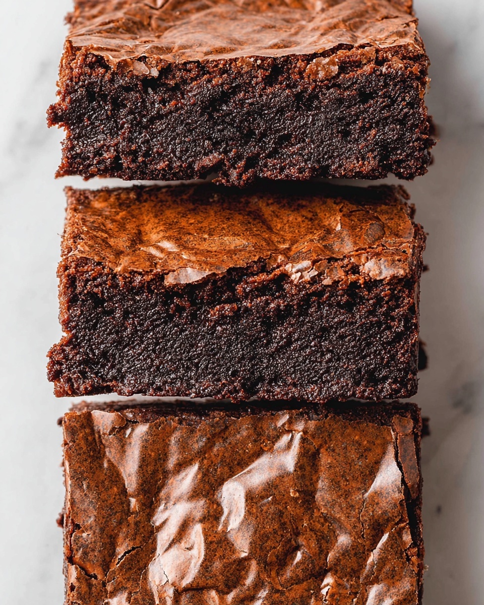 The image shows three large square-shaped pieces of chocolate brownie arranged vertically on a white marbled surface. Each brownie has a shiny, cracked, and wrinkled dark brown crust on top with a slightly rough texture. The inside layer beneath the crust is dense, moist, and rich dark brown, contrasting with the lighter, textured top. The brownies are placed close to each other, with the middle piece fully visible and the top and bottom pieces partially visible. Photo taken with an iphone --ar 4:5 --v 7