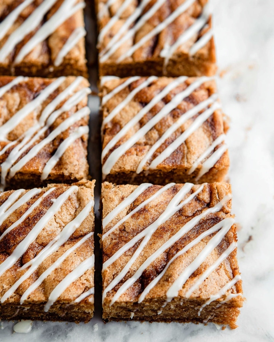 This image shows a close-up view of several square pieces of a baked dessert arranged neatly in rows on a white marbled surface. Each square has a golden-brown top layer with a slightly cracked texture and darker brown cinnamon swirls creating a patterned look. On top of each piece, there are white icing drizzles in thin diagonal lines, adding a glossy texture and contrast to the warm tones of the dessert underneath. The squares are cut evenly with clear, straight edges, and the focus is on the top surface textures and icing details. Photo taken with an iphone --ar 4:5 --v 7