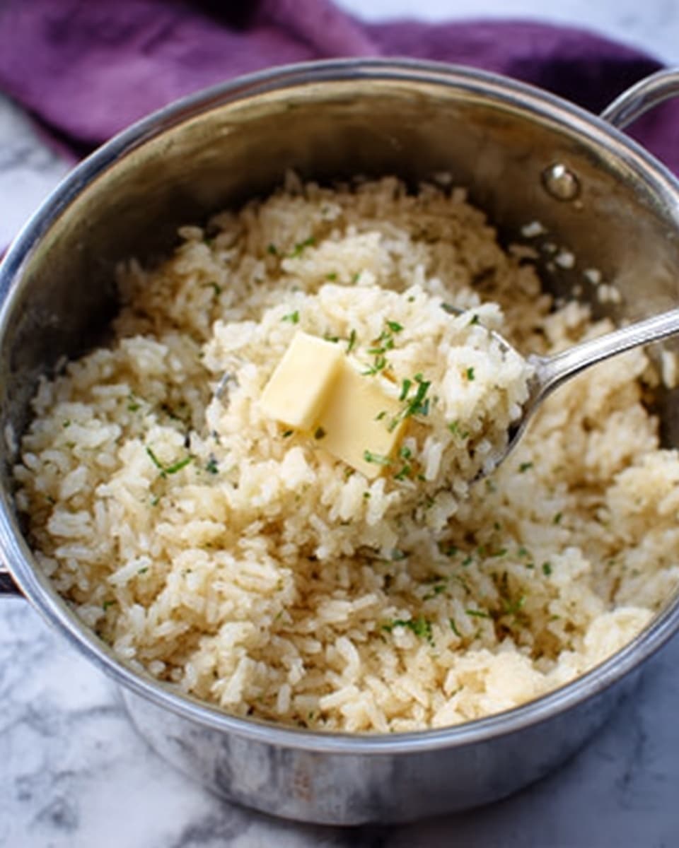 A close-up image of a shiny silver pot filled with cooked brown rice. A spoon inside the pot scoops up the rice, showing a cube of butter melting on top. The rice looks soft and fluffy with some small green herbs sprinkled around. The pot is on a white marbled surface, and the purple cloth is blurred in the background. Photo taken with an iphone --ar 4:5 --v 7