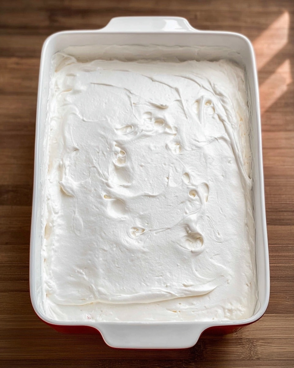 A white ceramic rectangular baking dish filled with a thick, smooth layer of white whipped topping spread evenly over the surface, showing soft texture marks and some small bubbles, sitting on a wooden surface with light reflection indicating its creamy consistency, with a white marbled texture as background photo taken with an iphone --ar 4:5 --v 7