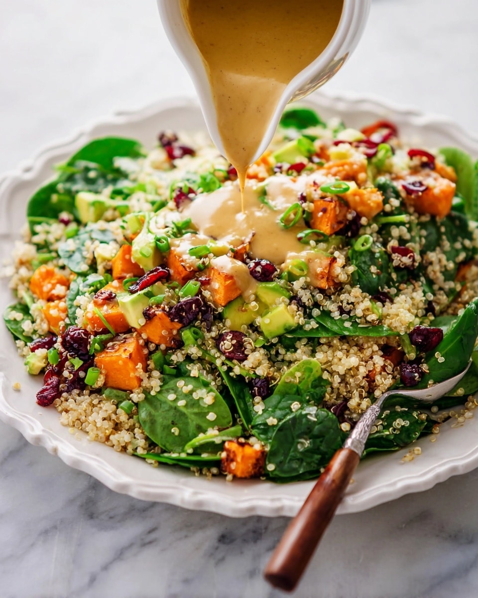 A white scalloped plate holds a layered salad with a base of light beige quinoa grains scattered throughout. On top of the quinoa are bright green spinach leaves, diced pieces of orange roasted sweet potato, dark red dried cranberries, small chunks of light green avocado, and finely sliced green onions. A smooth mustard-colored dressing is being poured from a white sauce boat over the salad, visibly spreading across the top, creating a creamy texture. A wooden spoon with a dark brown handle rests partially in the salad, lifting some ingredients. The plate is set on a white marbled surface. Photo taken with an iphone --ar 4:5 --v 7