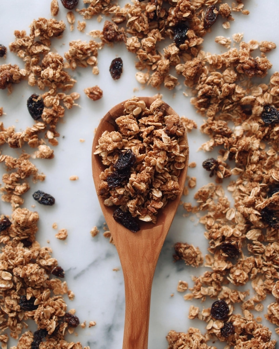 A wooden spoon is filled with clusters of granola made of light brown oat flakes mixed with small parts of darker nuts and dried dark raisins. The spoon lies on a white marbled surface scattered with more granola spread around it. The granola shows varying textures, with some pieces chunky and others loose, giving a natural, crunchy feel. Photo taken with an iphone --ar 4:5 --v 7