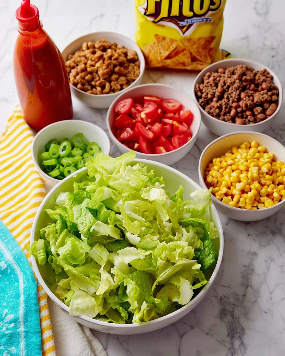 A white bowl filled with fresh green and pale green lettuce leaves forms the base layer at the front, with four smaller white bowls behind it containing seasoned ground beef, brown beans, yellow corn kernels, and chopped red tomatoes. A small white bowl with green onion pieces is also visible, while a yellow and white striped cloth is placed near the edge on a white marbled surface. A red bottle of salad dressing stands at the left, and a bright yellow bag of Fritos chips stands at the back. photo taken with an iphone --ar 4:5 --v 7