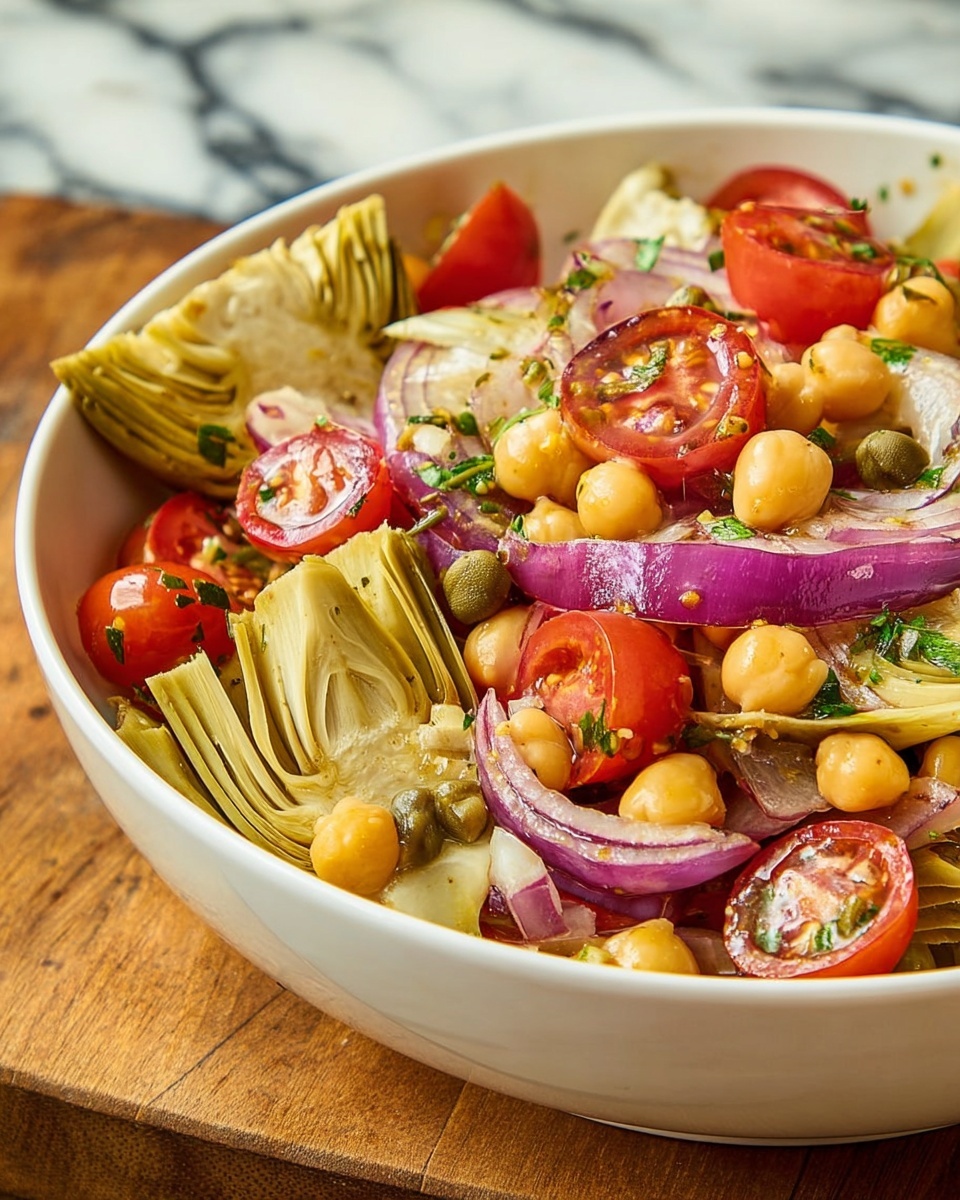 The image shows a white bowl filled with a colorful salad placed on a wooden table with a burnt orange cloth nearby. The salad has layers starting with sliced red cherry tomatoes and light yellow artichoke hearts scattered evenly on top. There are thin slices of purple-red onion curling through the salad, along with beige chickpeas adding round shapes throughout. Small green herbs are sprinkled on top, providing a fresh contrast. A silver fork is placed inside the bowl on the right side. Nearby, there are small dishes containing chopped green herbs and fresh green leaves. The background surface is white marbled. Photo taken with an iphone --ar 4:5 --v 7