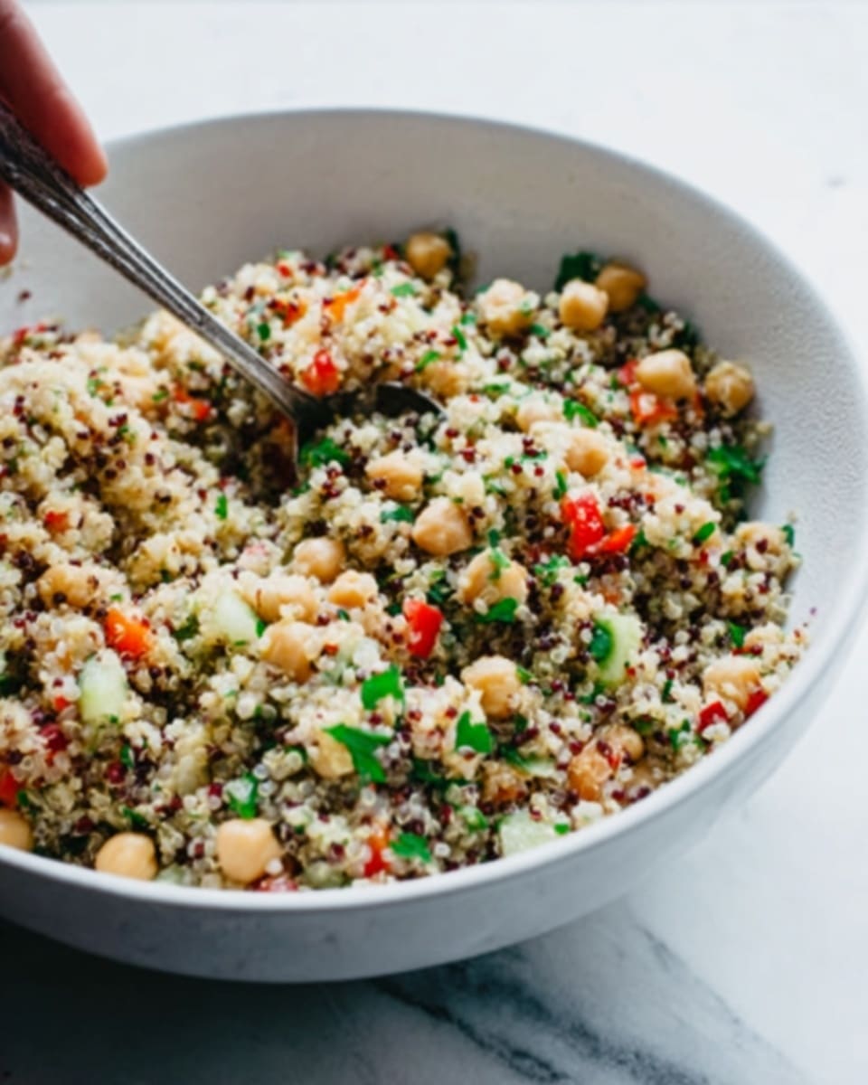 A close-up view of a quinoa salad in a white bowl on a white marbled surface, showing a mix of small, round quinoa grains in light beige and dark brown colors evenly spread throughout. Mixed with the quinoa are visible layers of diced cucumbers with light green and dark green skin, small pieces of red bell pepper, finely chopped red onions, whole light beige chickpeas, and chopped fresh dark green parsley scattered throughout. The textures range from the soft quinoa grains to the crunchy and fresh vegetables, all combined to create a colorful and fresh look. photo taken with an iphone --ar 4:5 --v 7