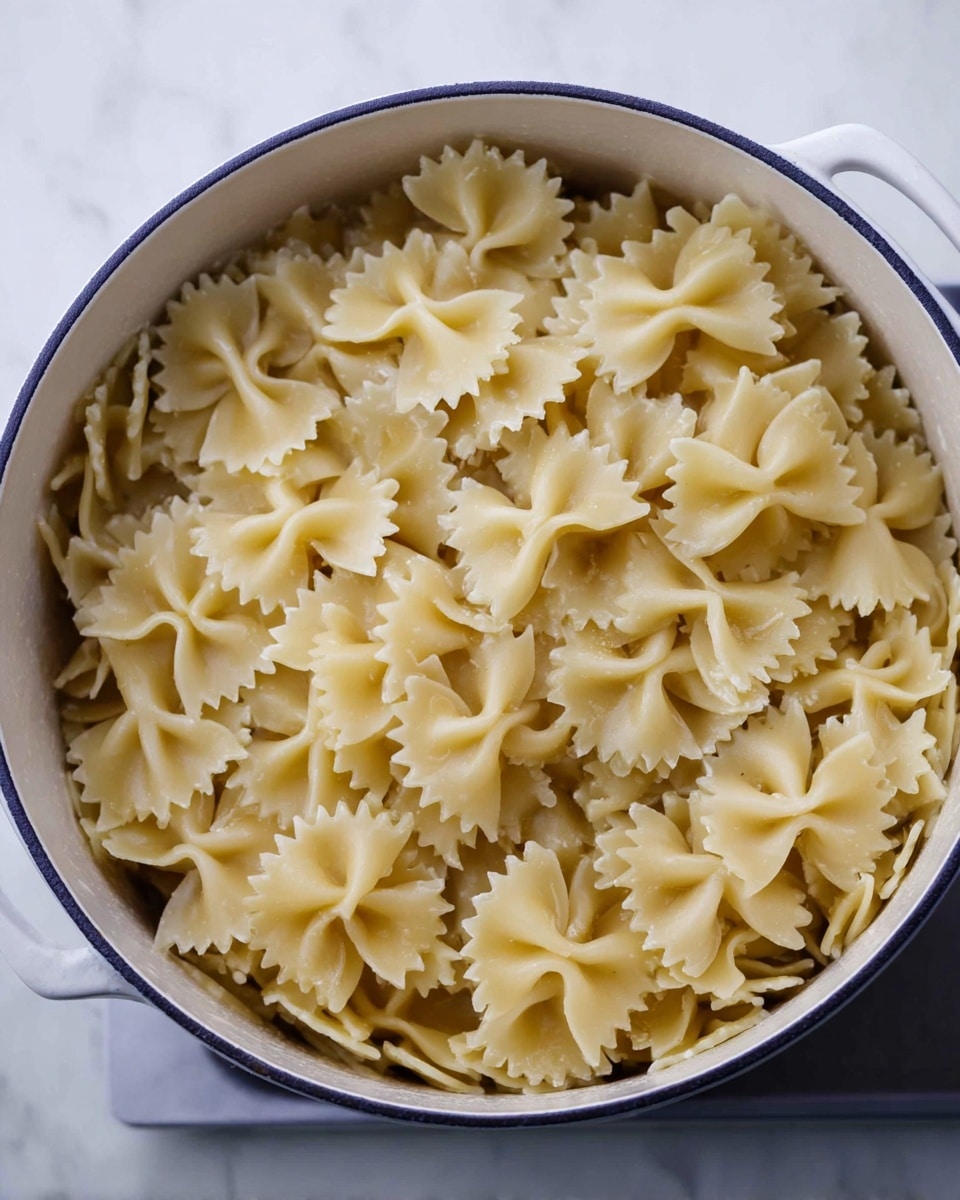 A white pot filled with a single layer of cooked farfalle pasta, light yellow in color with a slightly soft texture, the pasta pieces showing their bow-tie shape with ruffled edges. The pot is on a white marbled surface, and the inside of the pot is also white, contrasting with the pale pasta inside. Photo taken with an iphone --ar 4:5 --v 7