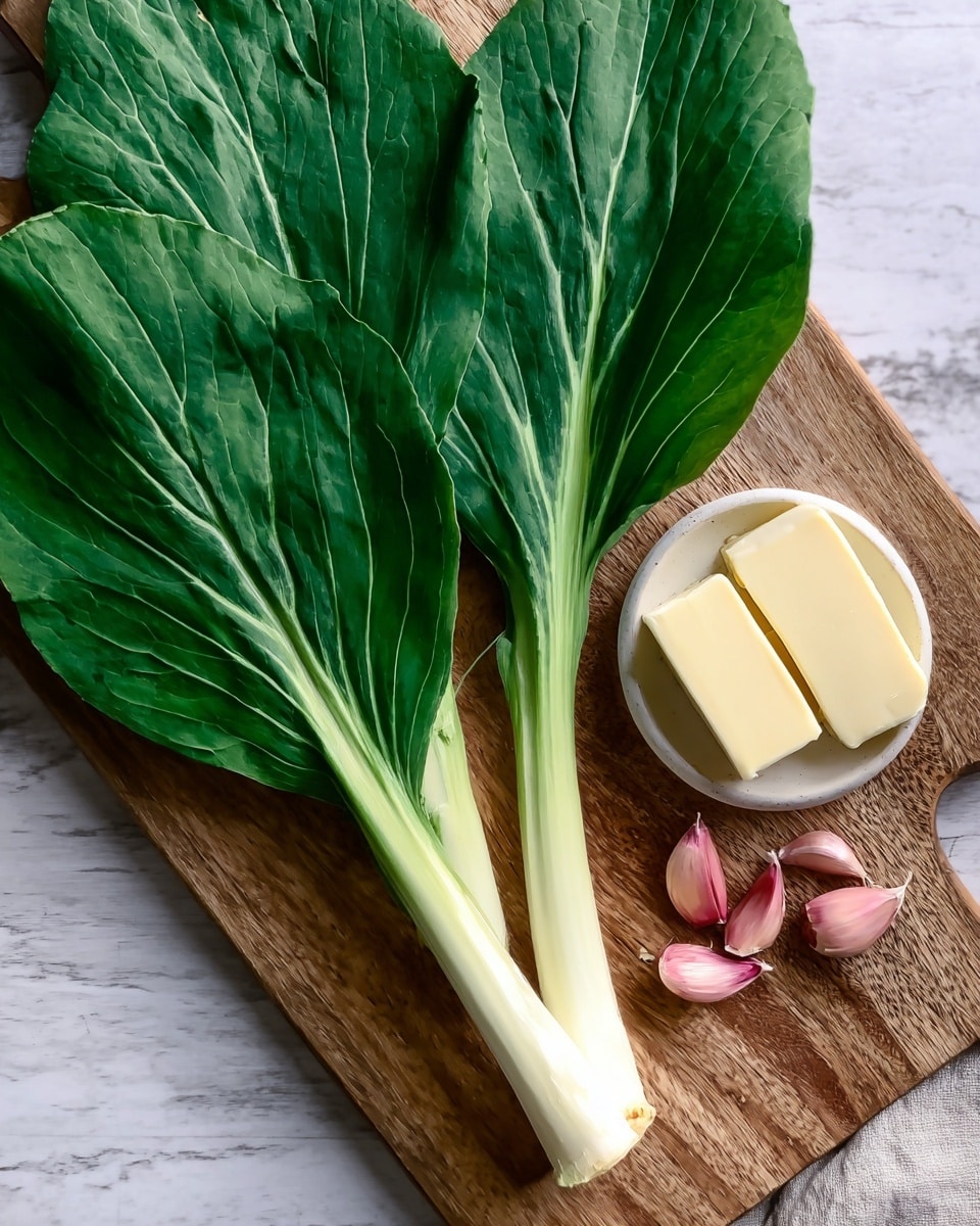 The image shows three fresh green leaves with thick white stems placed on a wooden cutting board. Next to the leaves, there are three cloves of garlic with a pinkish outer skin. Below the garlic, there is a small white bowl holding two rectangular pieces of pale yellow butter. The background is a white marbled texture. Photo taken with an iphone --ar 4:5 --v 7