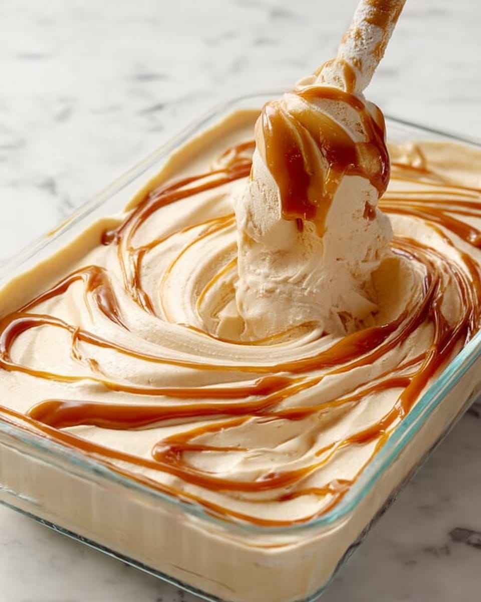 A close-up view of a clear rectangular glass dish filled with creamy light beige ice cream with smooth, fluffy texture, with rich caramel-colored syrup swirled on the top, creating flowing, curved lines and swirls all over the surface. A utensil covered in the same ice cream and syrup mixture is held above the dish, showing the mixture lifting and swirling in the air. The dish sits on a white marbled texture surface. photo taken with an iphone --ar 4:5 --v 7