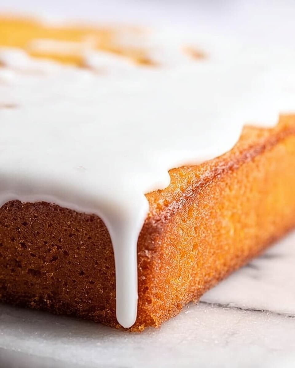 The image shows a close-up of a square piece of golden-brown cake with a smooth texture on top and slightly darker edges. On the top right corner of the cake, a thick layer of shiny white icing is spread, dripping slightly over the edge. The cake sits on a white marbled surface, enhancing the warm tones of the cake and the bright white icing. The image captures the cake from a low angle, focusing on the sharp edges and details of the icing and cake crust. photo taken with an iphone --ar 4:5 --v 7