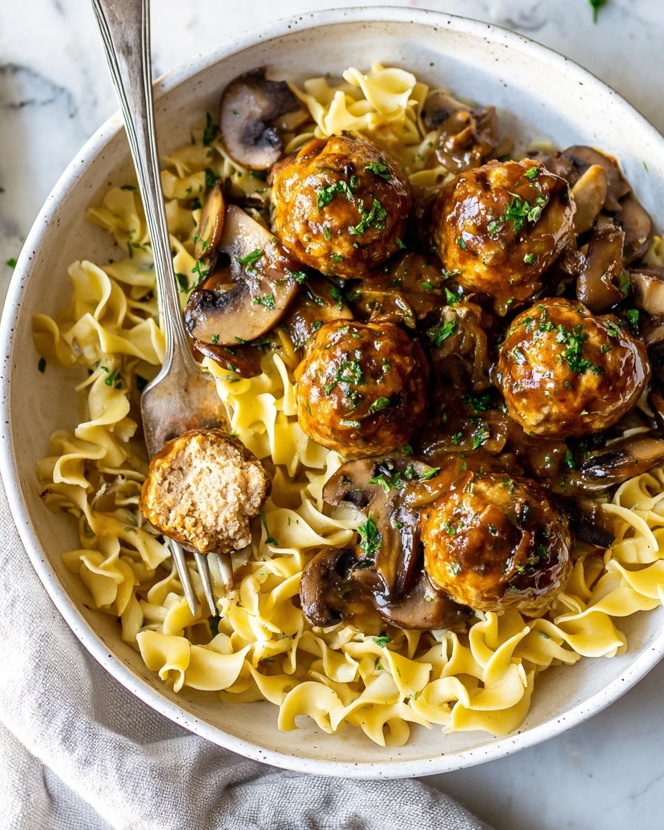 A silver pan filled with about twenty golden-brown meatballs arranged evenly in rich reddish-brown sauce with visible herbs. Thinly sliced mushrooms float among the meatballs, some partially covered in sauce. The pan sits on a white marbled surface, with a beige plate of yellow curly pasta partly in view on the bottom right side. The scene is bright and sharp with a close-up focus. photo taken with an iphone --ar 4:5 --v 7