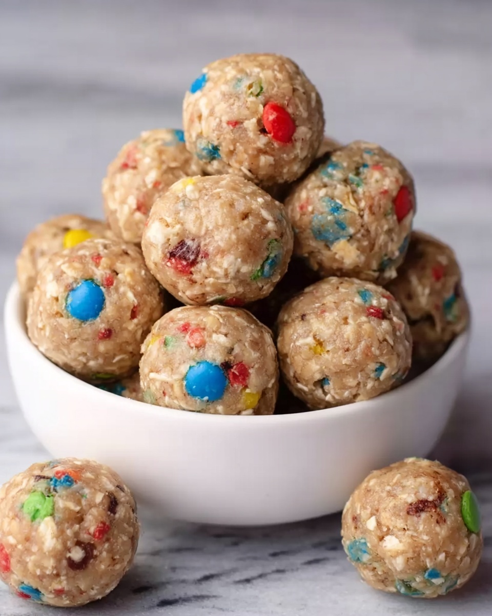 The image shows close-up round snack balls made from oats and small colorful candy pieces mixed inside. The balls have a rough texture due to the oats and have colors like red, orange, blue, yellow, and green from the candies scattered throughout. They are placed on a dark surface with some balls in the background slightly out of focus, giving depth to the image. The main ball in front is centered and sharp, showing its detailed texture clearly. Photo taken with an iphone --ar 4:5 --v 7