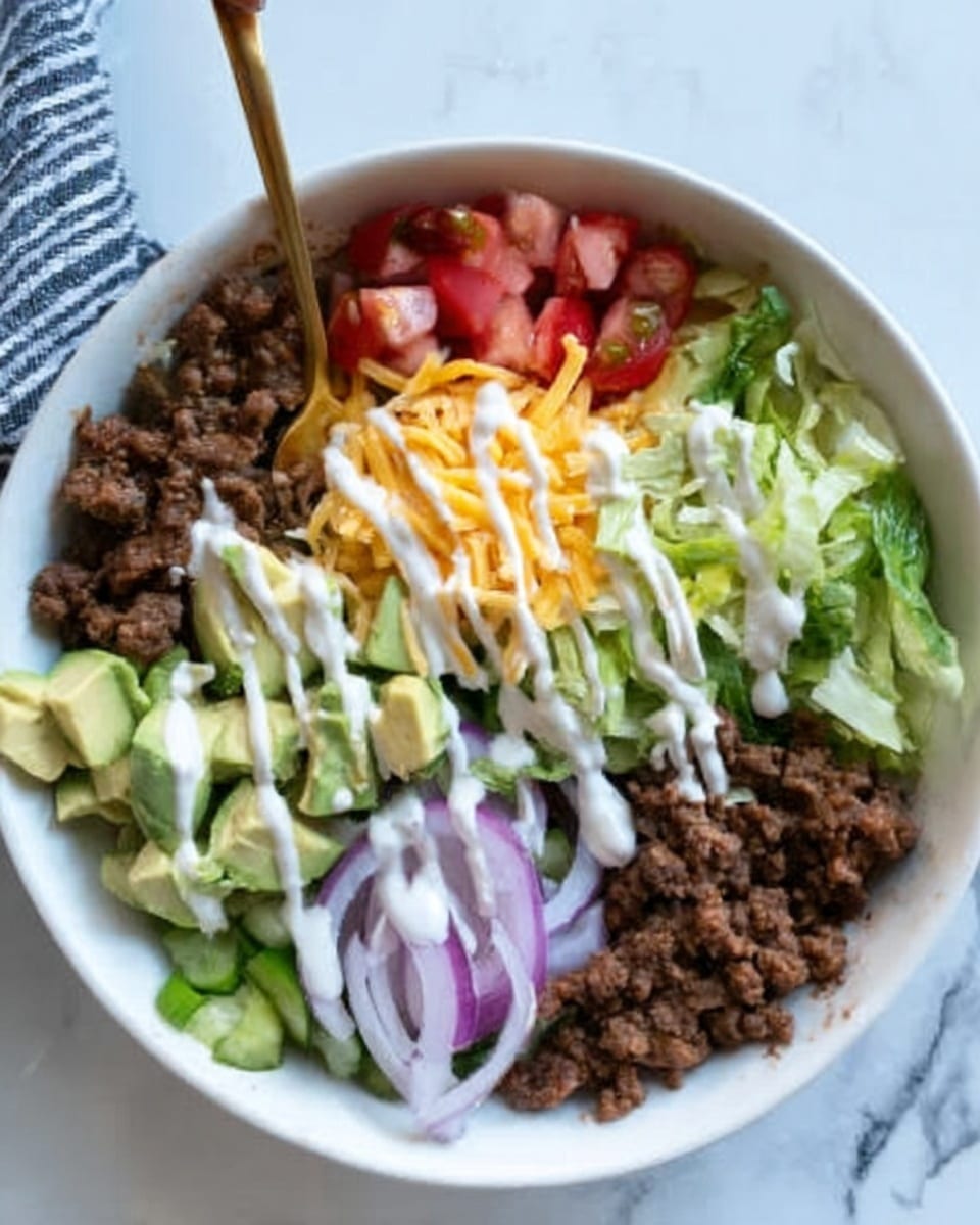 A white bowl holds a layered taco salad arranged in sections on a bed of chopped green lettuce. Starting from the left, there is a pile of brown cooked ground beef topped with white creamy dressing drizzled over it. Next to it is diced green pickles, followed by diced light green avocado with light pink creamy dressing on top. To the right, thinly sliced red onions create a ringed layer, and next to them is a mound of shredded yellow cheddar cheese. At the bottom right, diced red tomatoes lie over more chopped lettuce with white dressing drizzled across the salad. A gold spoon rests inside the bowl on a white marbled surface with a black and white striped cloth partially visible behind. Photo taken with an iphone --ar 4:5 --v 7