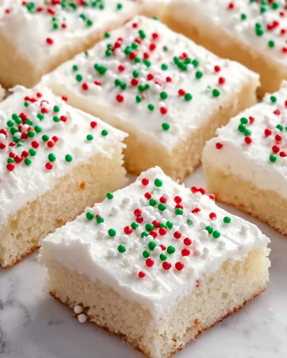 The image shows several square pieces of soft white cake, each topped with a thick, smooth layer of white frosting. On the frosting, tiny red, green, and white round sprinkles are evenly spread, adding small bursts of color. The cake itself looks light and fluffy with a soft texture visible on the sides. The pieces are closely placed on a white marbled surface, showing clear details of the frosting and sprinkles. photo taken with an iphone --ar 4:5 --v 7