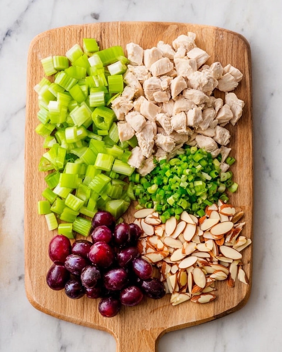 A wooden cutting board is placed on a white marbled surface, with five neatly arranged rows of ingredients. From left to right, there is a pile of bright green celery cubes, followed by a larger pile of light beige cooked diced chicken pieces. Next to it is a small pile of finely chopped green onions, then a group of halved dark purple grapes, and finally a row of light brown slivered almonds. The scene is well lit with natural light, highlighting the fresh colors and textures of each ingredient. Photo taken with an iphone --ar 4:5 --v 7